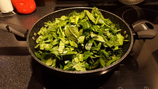 spinach piled high in the pan spinach added to pan