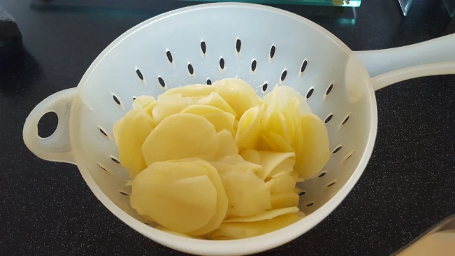 sliced potatoes in a colander for smoked haddock bacon bake sliced potatoes